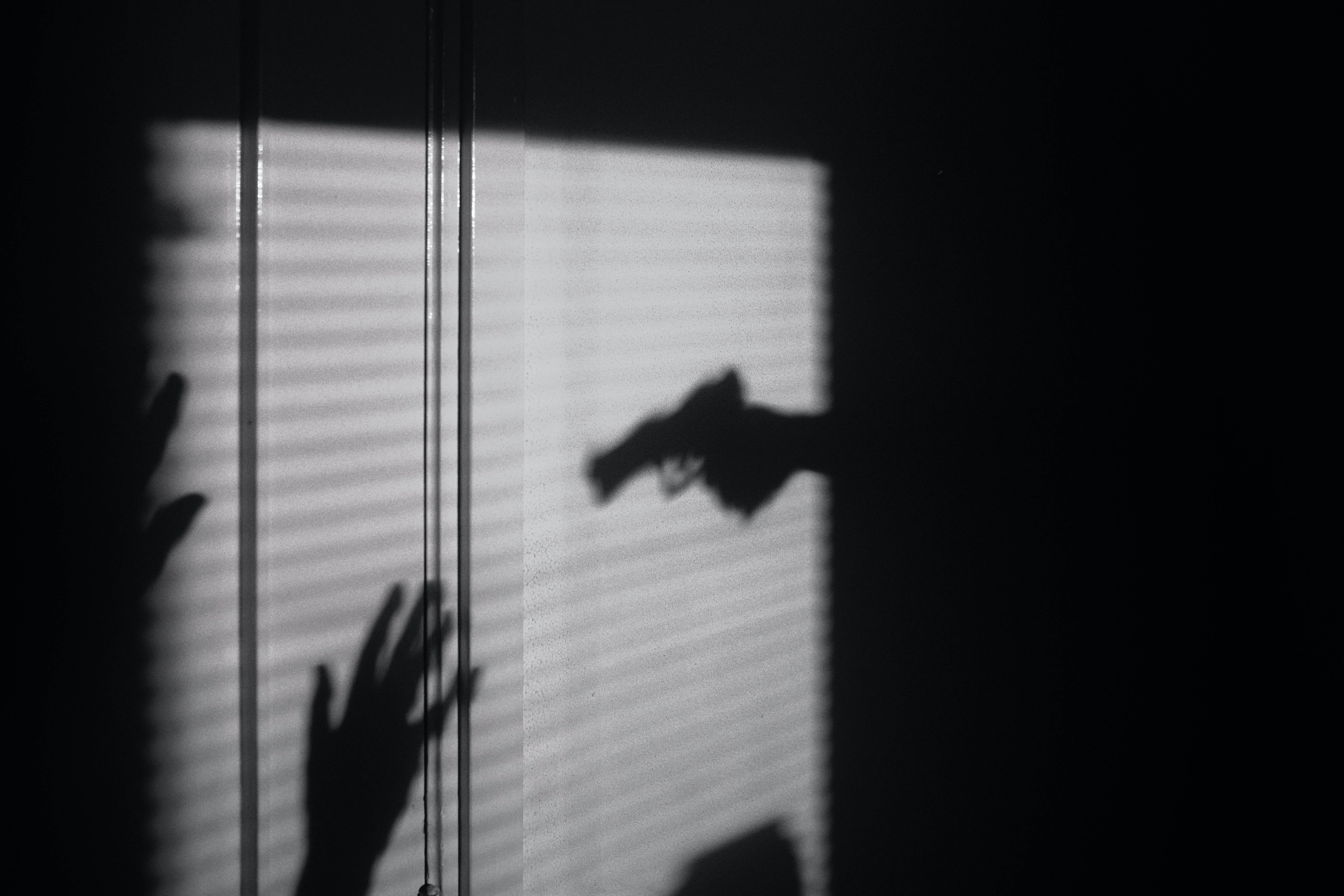 A window of light silhouettes a person holding a gun intimidating another shadowy figure.